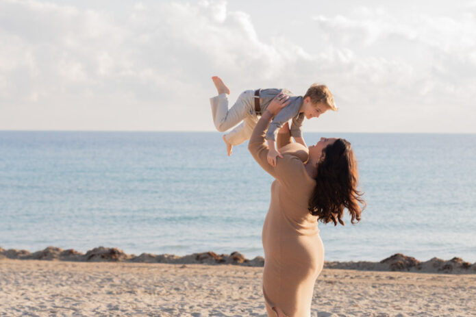 mother lifting son in the air on beach