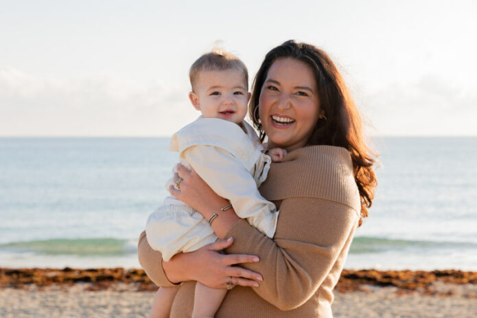 mother holding baby and smiling at camera on beach