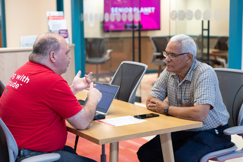 Senior Planet staff member helping a member with a laptop during one-on-one tech help